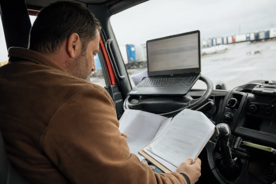 Właściciel firmy transportowej sprawdza w laptopie w kabinie ciężarówki obwieszczenie o upadłości przedsiębiorcy, któremu wystawił faktury